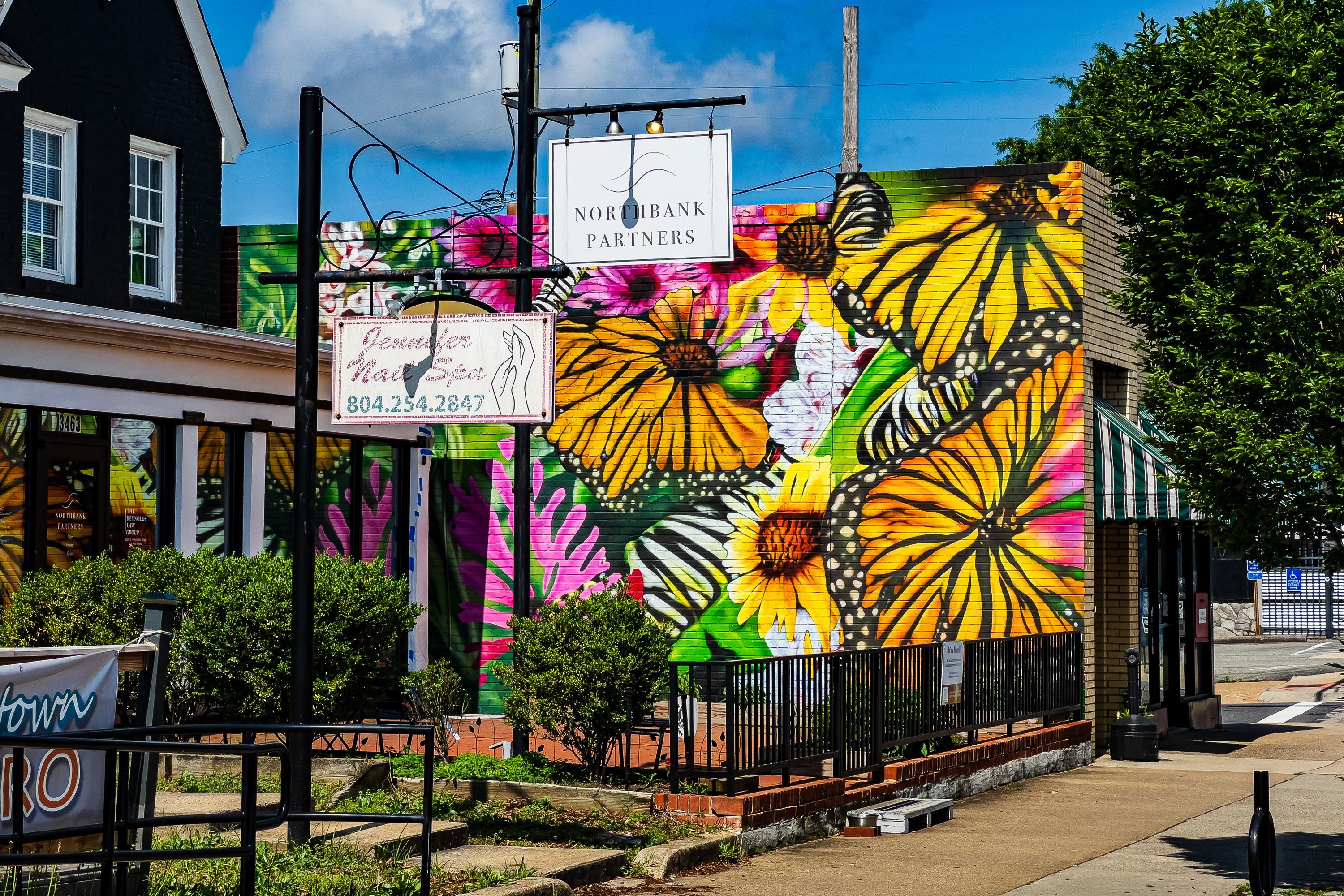 The finished mural on the red brick wall beside Northbank Partners, oversized monarch butterflies on yellow and pink flowers, the hanging Northbank sign in front of it