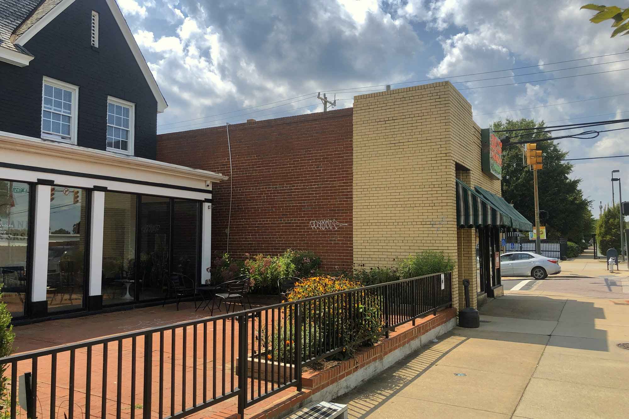 The wall before painting, bare red brick with a white graffiti tag on it and the monarch waystation planted along its base