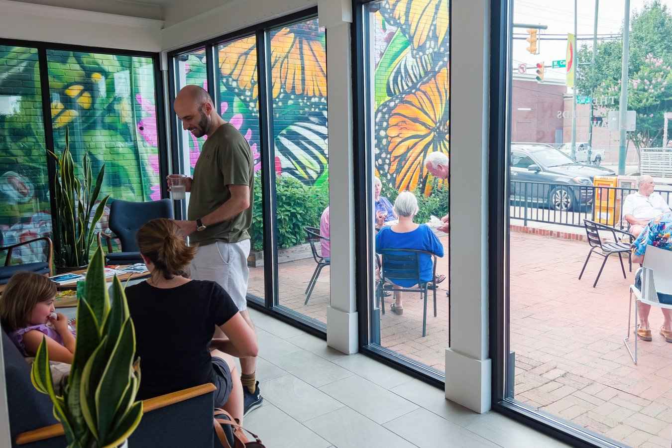 The mural seen from inside the office through the floor to ceiling glass, with clients sitting on the patio in front of it