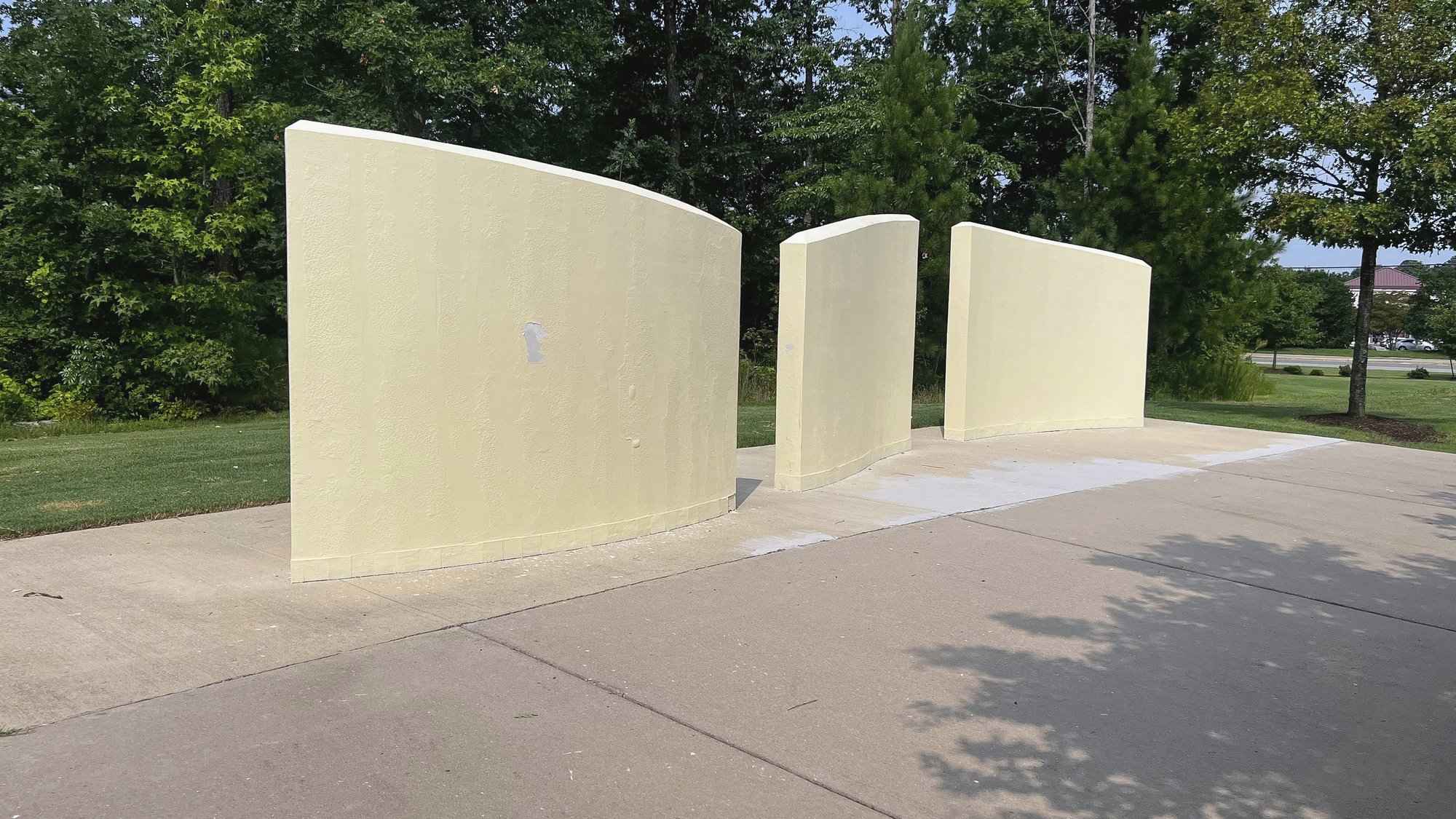 The three concrete walls before painting, the old yellow paint peeling in patches, in the middle of the park
