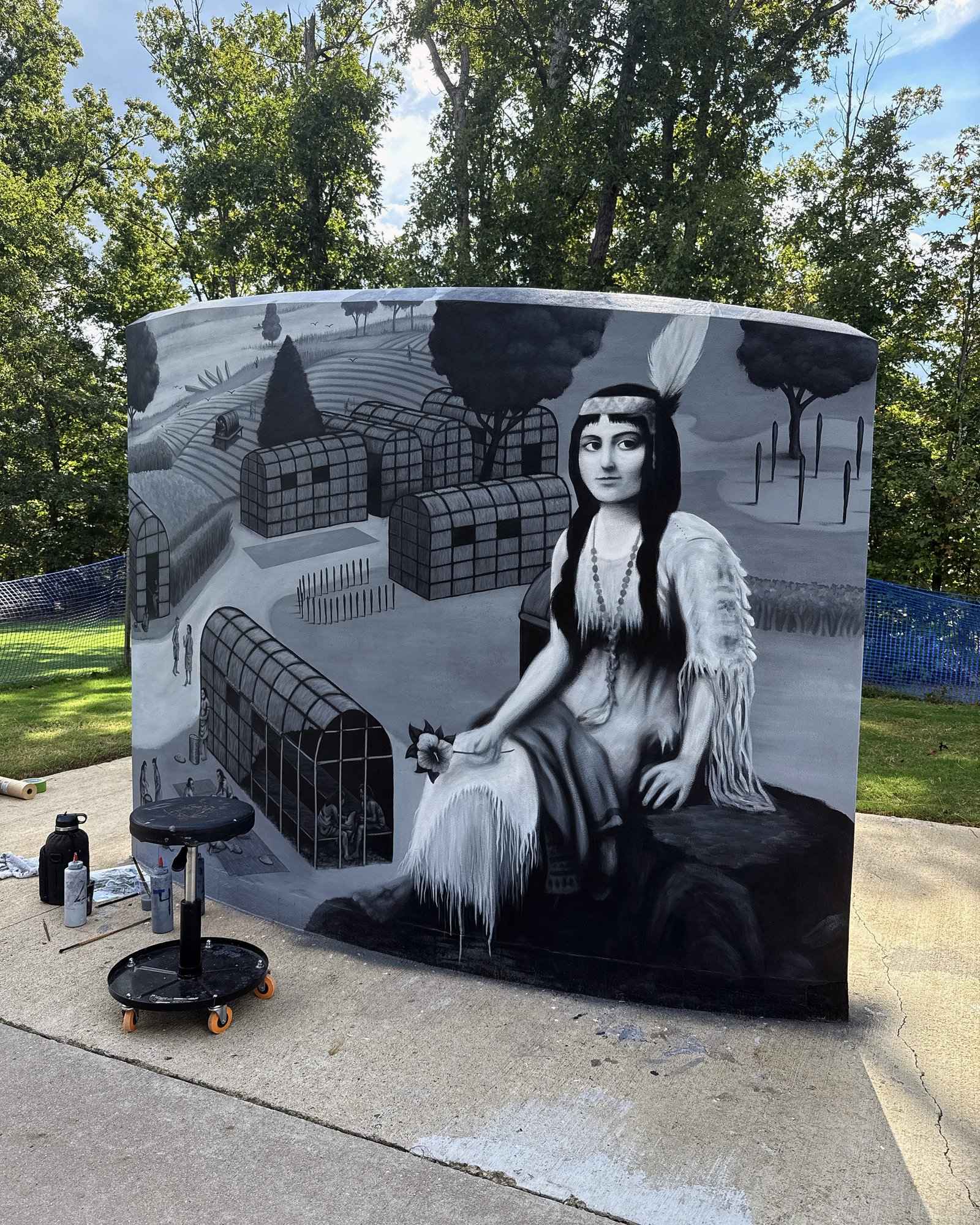 The wall painted from old engravings and maps, a Native woman and a village in grayscale, the painting wrapping around the end of the wall