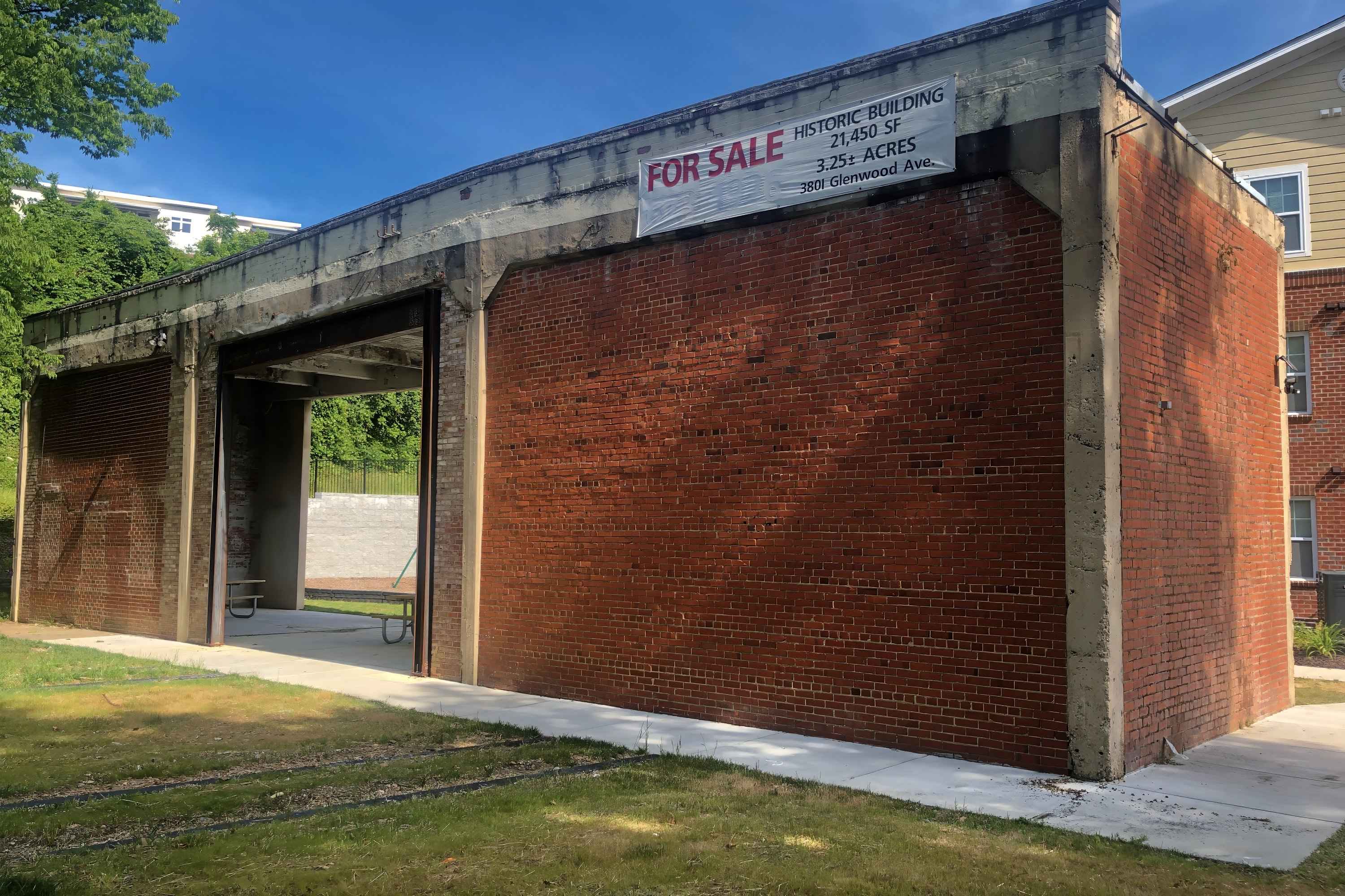 The preserved bay of the trolley barn before painting, bare brick with a For Sale sign
