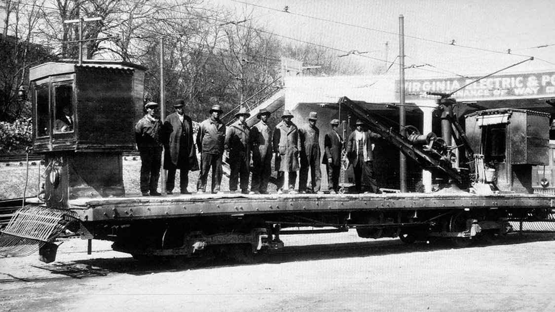 The 1925 photograph in full: the Virginia Electric & Power Co. maintenance crew on the flatcar outside this barn, the sign on the wall behind them